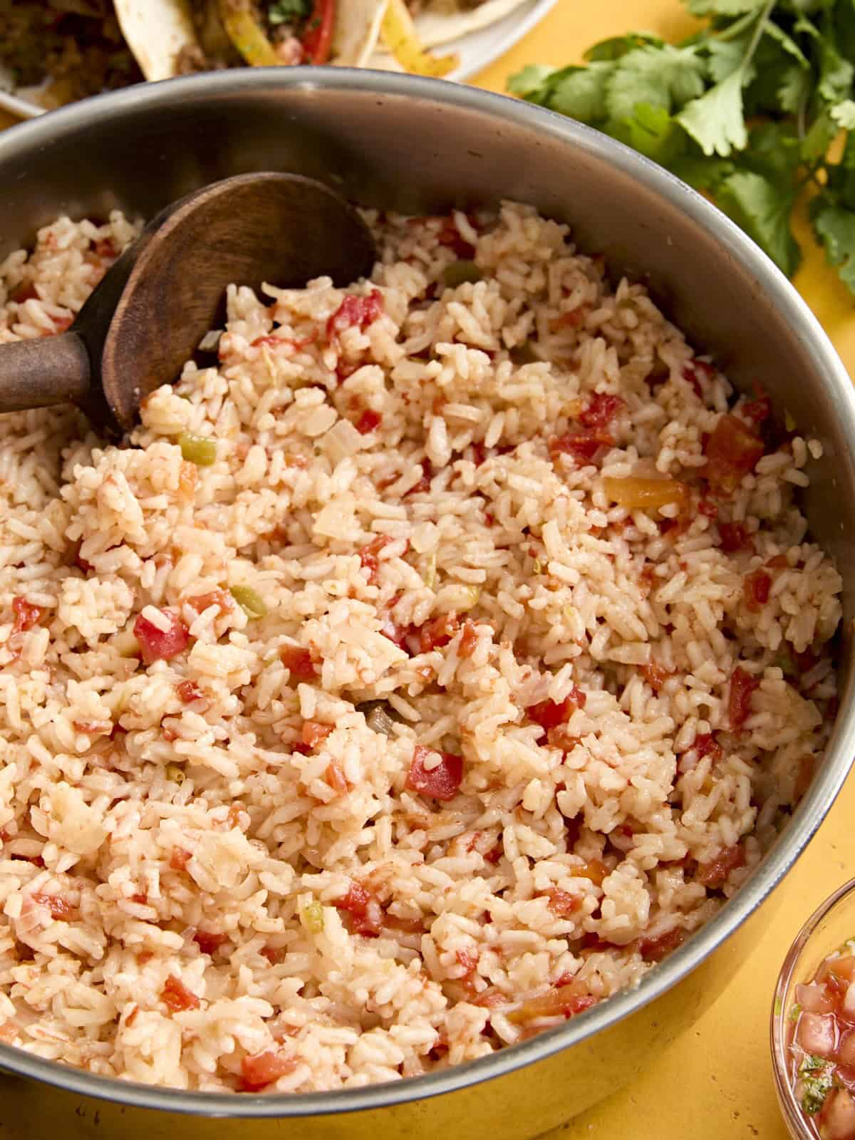 Side view of spanish rice in a skillet with a wooden spoon.