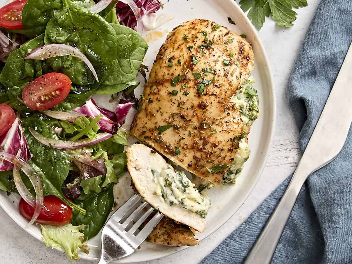 spinach stuffed chicken breasts on a plate served alongside a side salad.