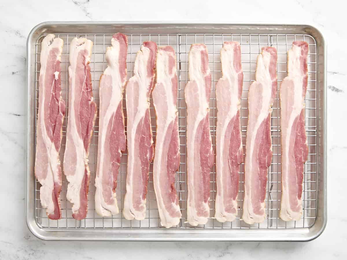 Raw bacon on a wire rack over a parchment lined baking sheet.