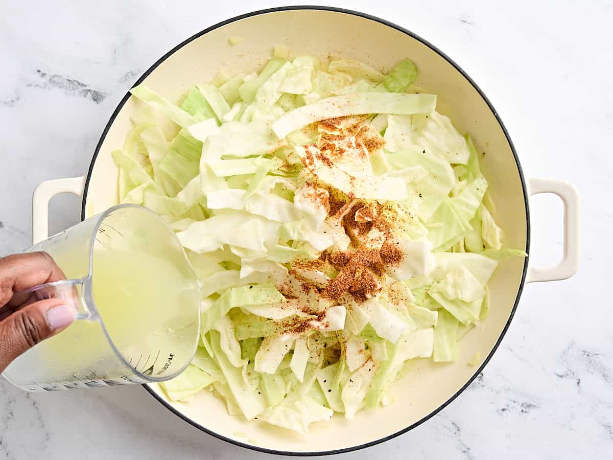 Chicken broth and creole seasoning added to sauteed cabbage in a skillet.