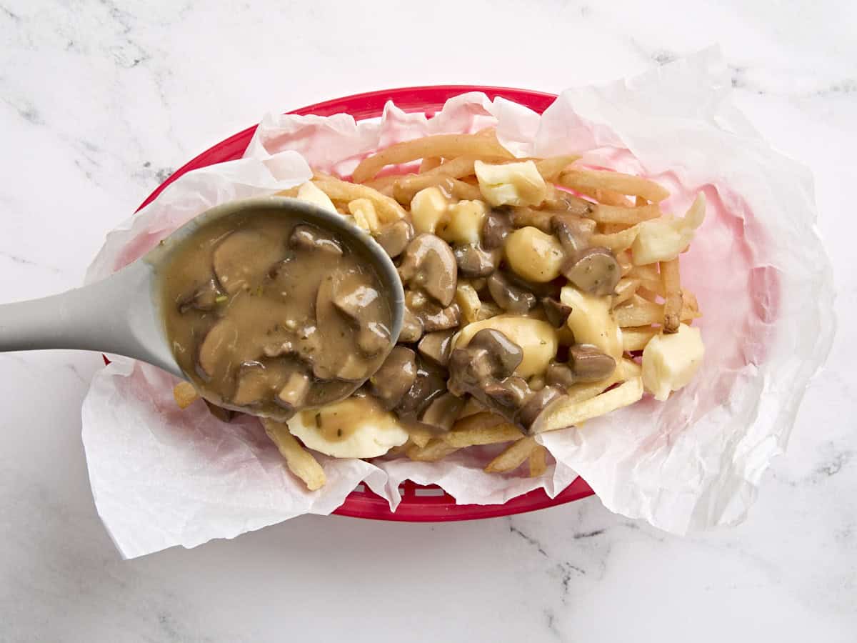 A basket of french fries and cheese curds being topped with mushroom gravy to make poutine.