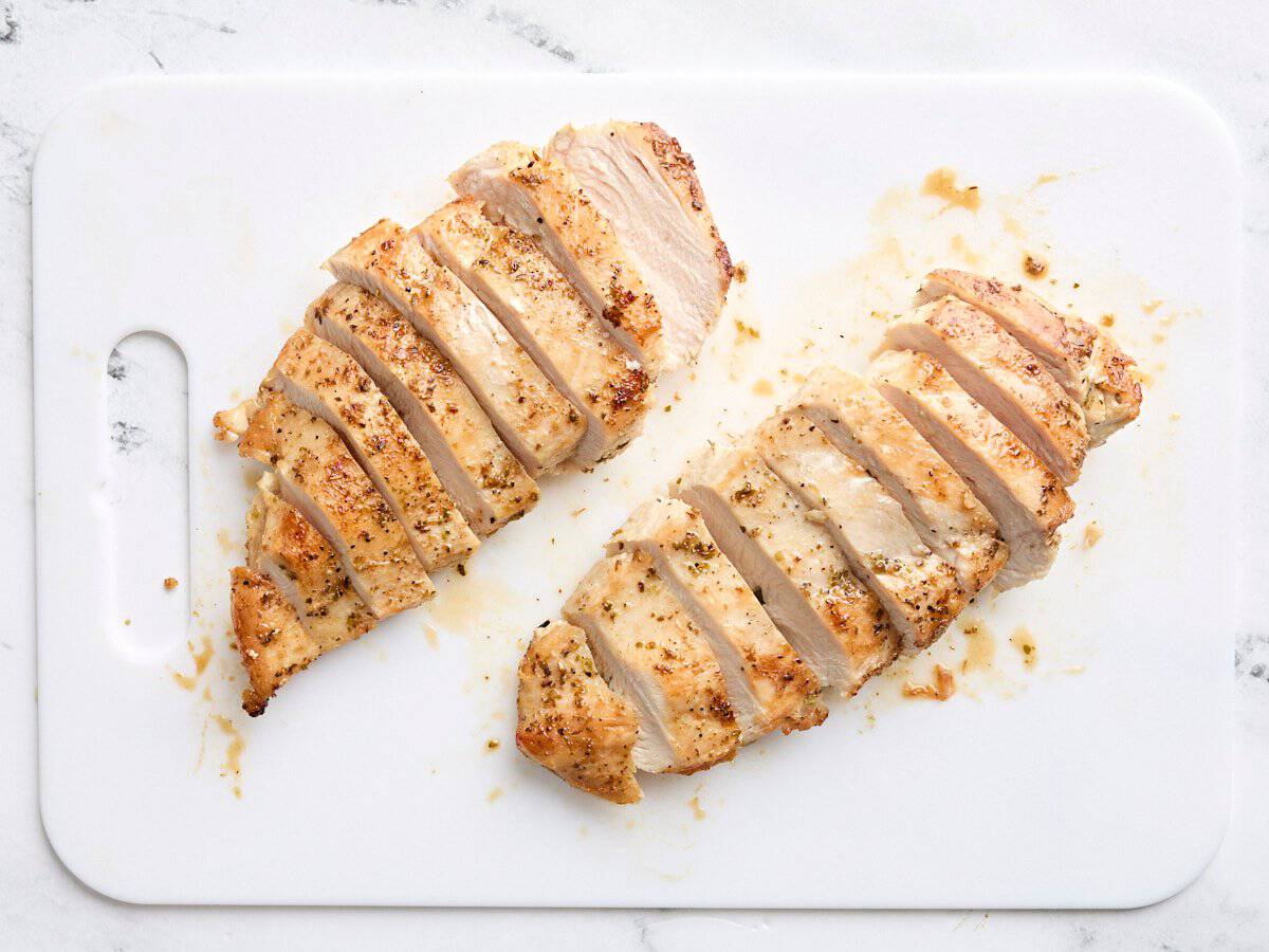 Sliced cooked chicken breast on a cutting board.