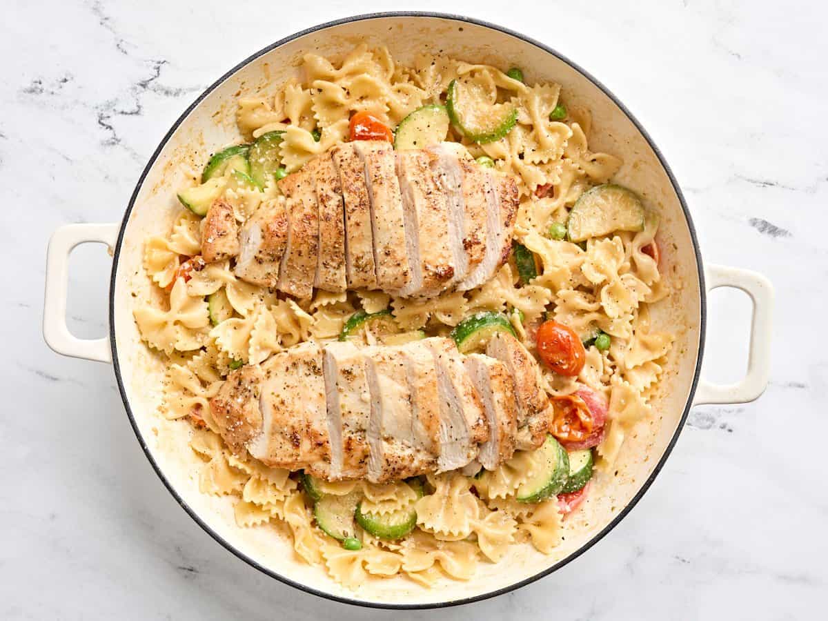 Pasta Primavera with chicken breasts placed on top in a skillet.