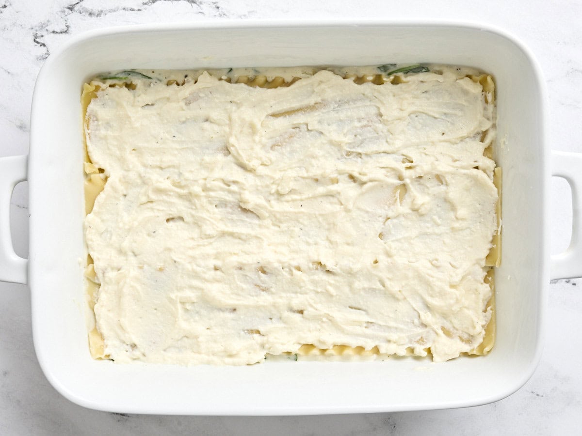 A layer of ricotta cheese and spinach mix added on top of lasagna sheets in a baking dish.