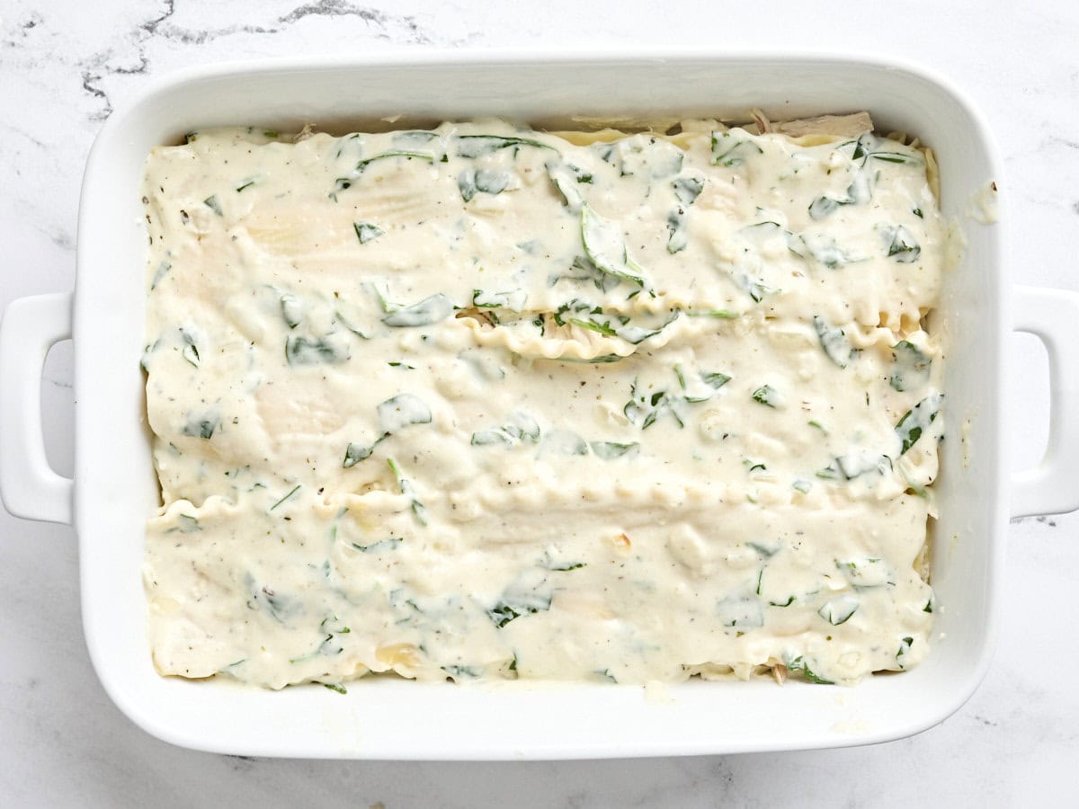 Another layer of ricotta cheese and spinach mix added on top of lasagna sheets in a baking dish.