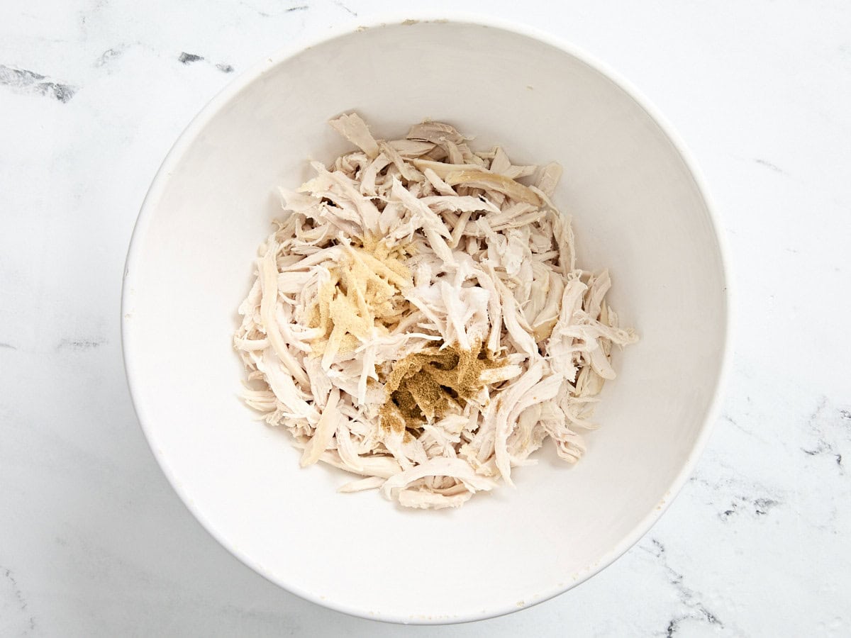 Shredded chicken added to a bowl with seasonings.