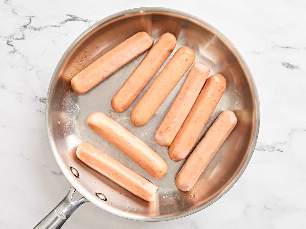 Raw sausages in a skillet.