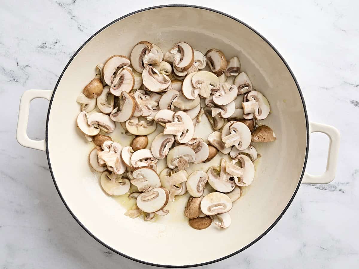 Sliced mushrooms sauteing in a deep skillet.