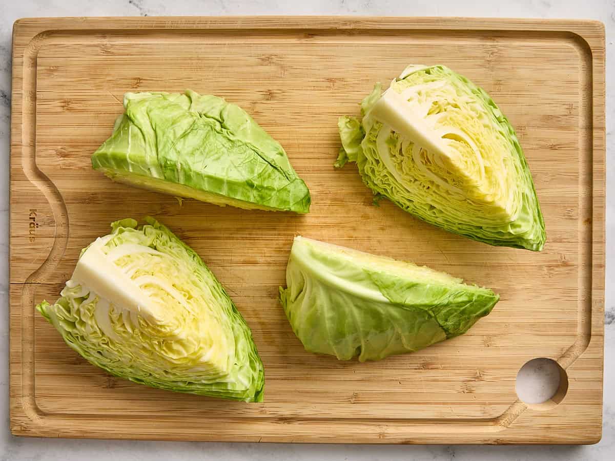 A head of cabbage cut into four wedges on a wooden cutting board.