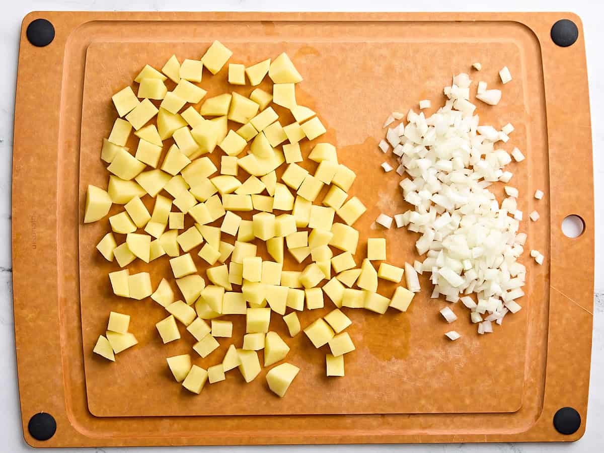 Diced potatoes and diced onion on a wooden cutting board.