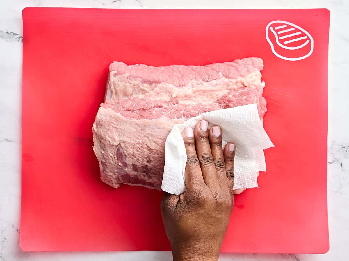 A hand blotting a piece of corned beef with a paper towel.