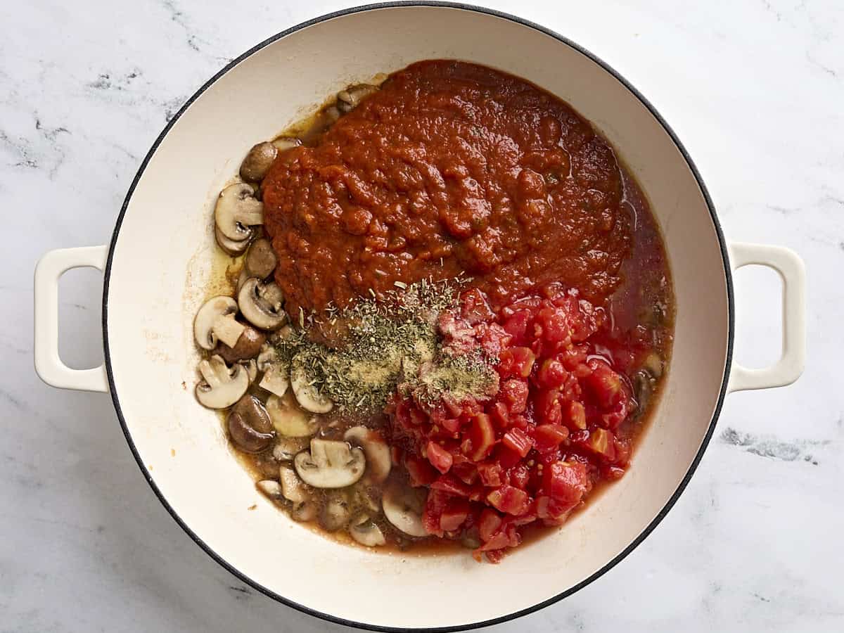 Marinara sauce, diced tomatoes, and seasonings added to a skillet with sliced mushrooms.