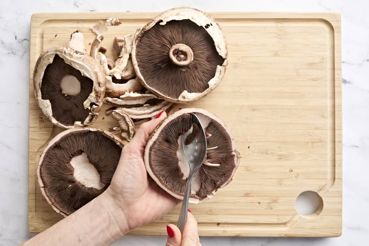 A spoon scooping the gills out of a portobello mushroom.