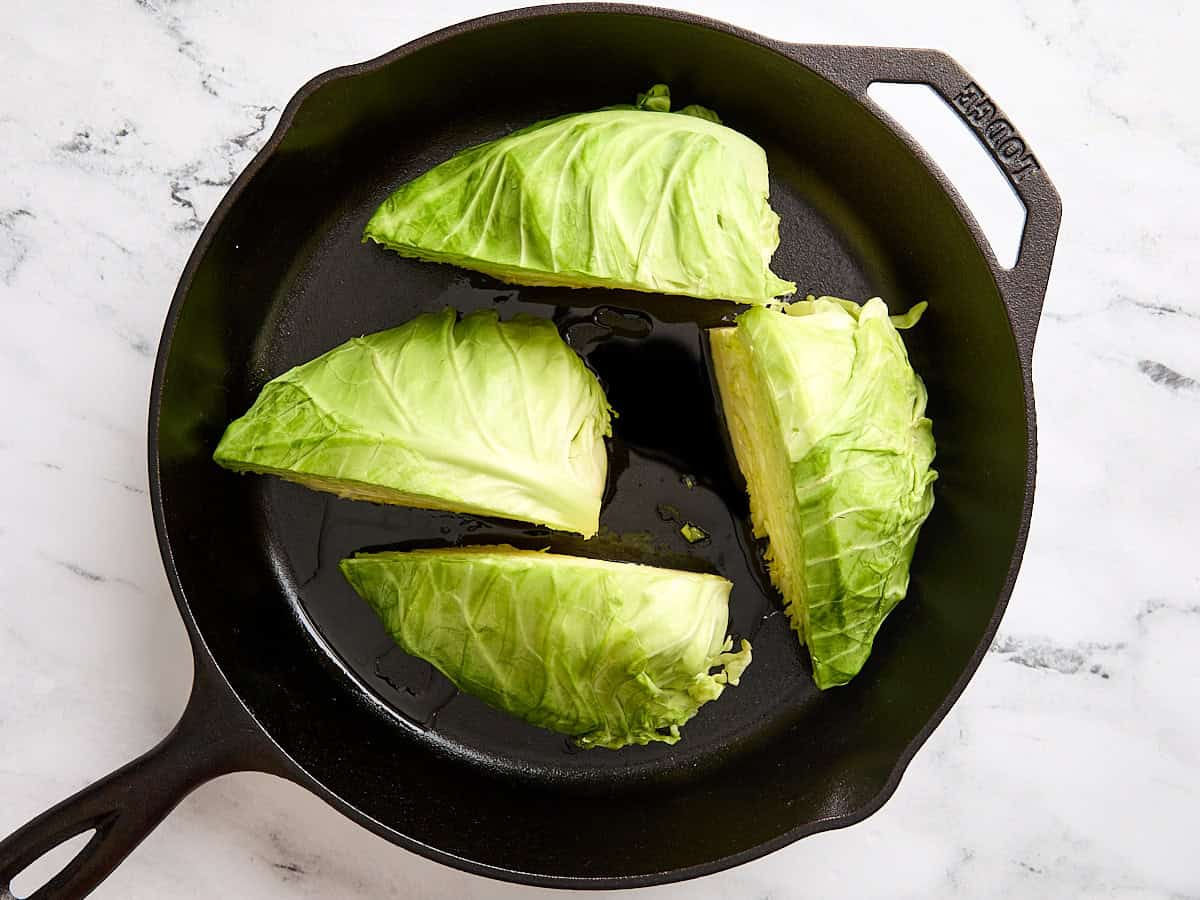 Cabbage steaks searing in a cast iron skillet.