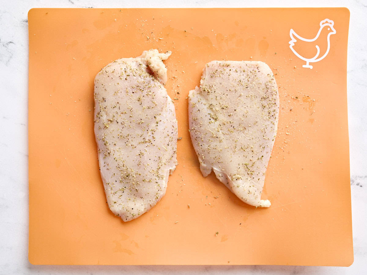 Seasoned chicken breasts on a cutting board.