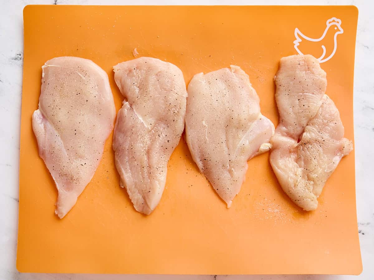 Seasoned chicken breasts on a cutting mat.