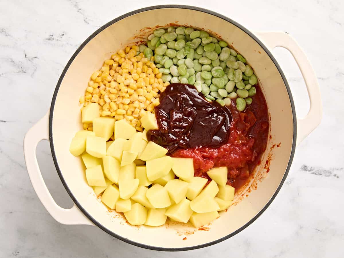 Frozen lima beans, frozen corn, bbq sauce, canned tomatoes, and diced potatoes added to a pot.