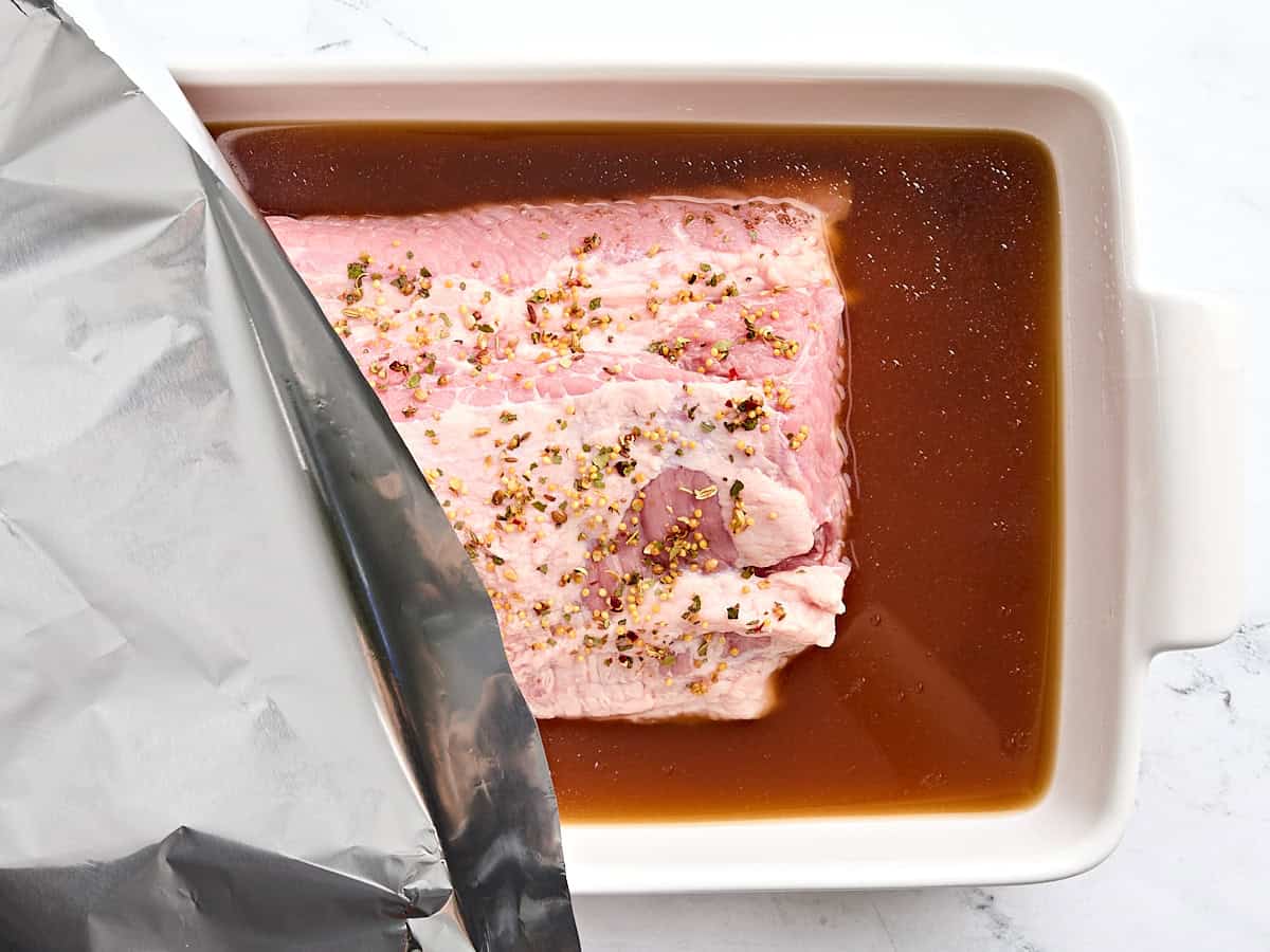 A piece of foil being added on top of corned beef in a baking dish.