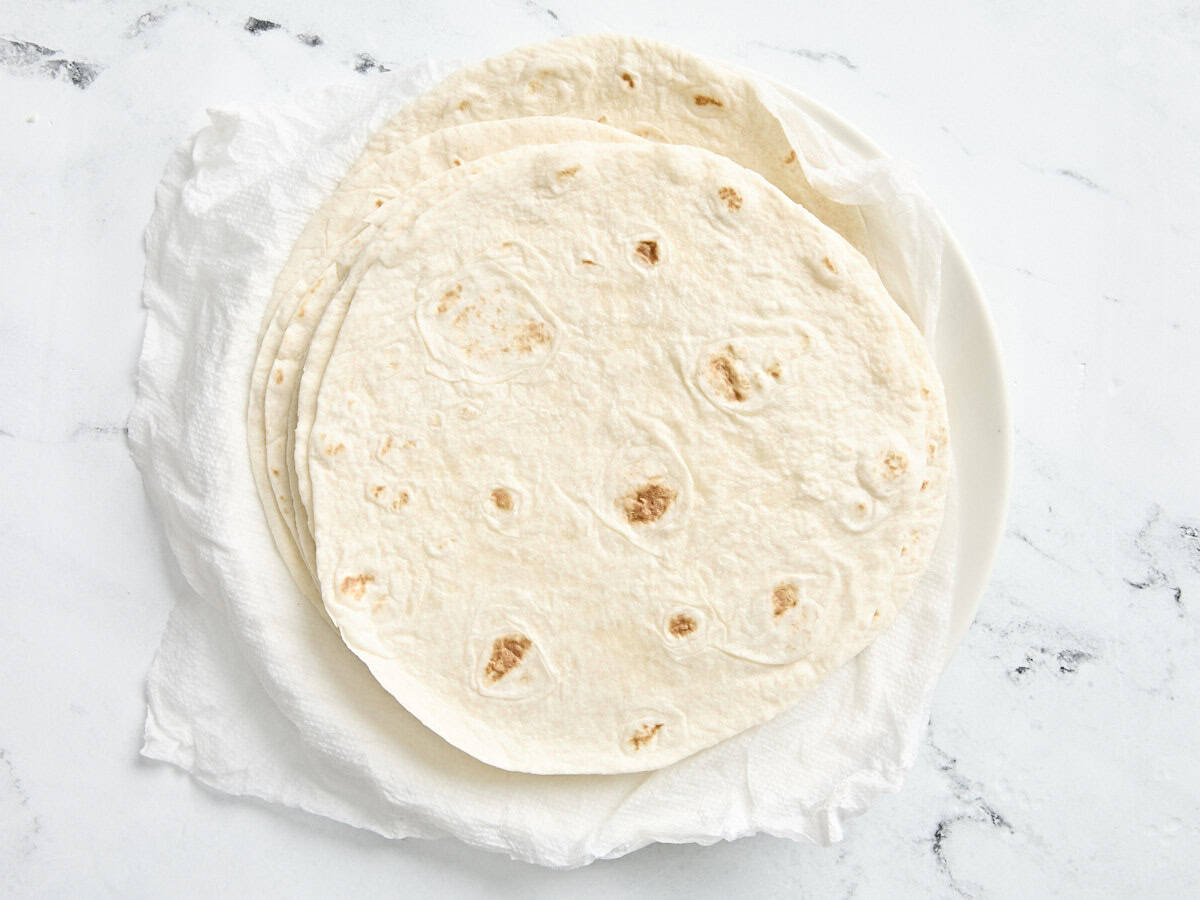 A pile of flour tortillas on a paper towel lined plate.