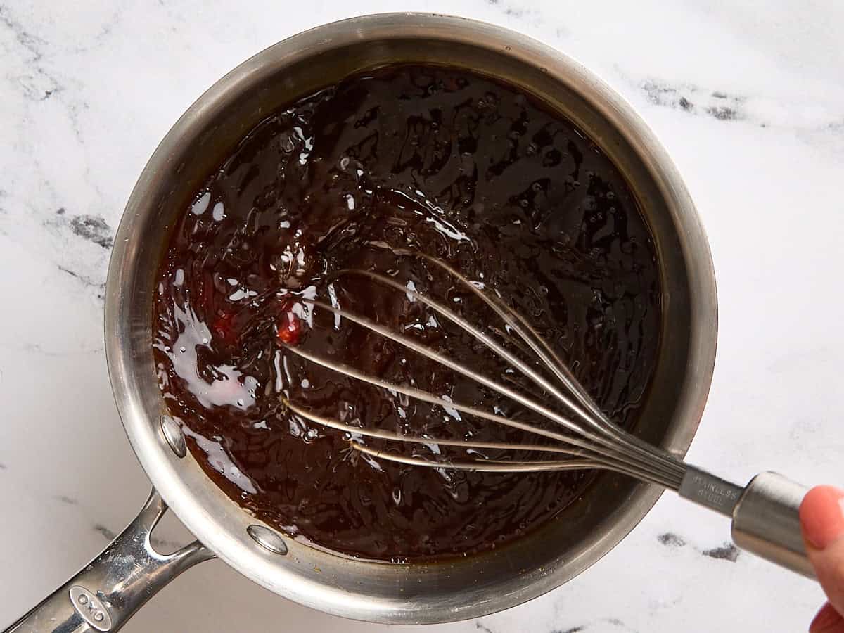 A whisk mixing together a sauce for cabbage steaks in a sauce pan.