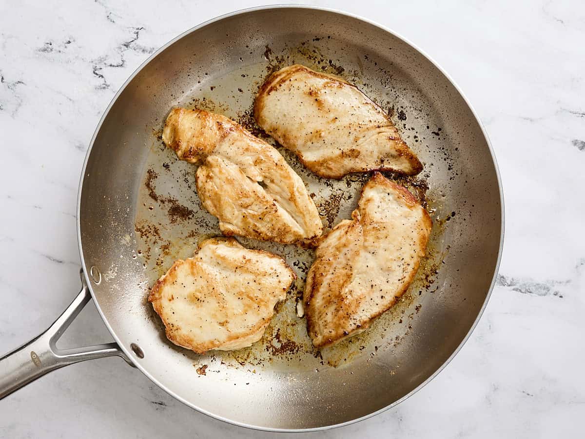 Chicken breasts cooking in a skillet.