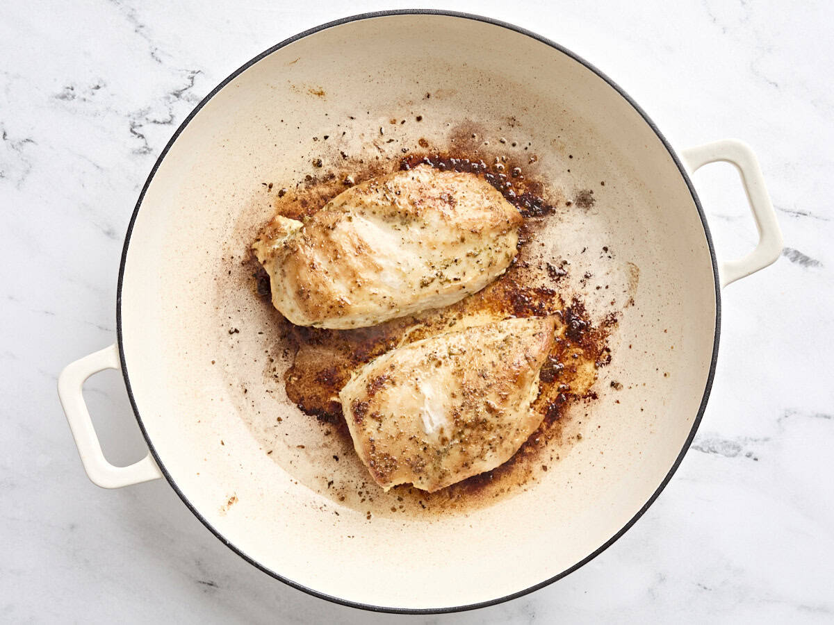 Two chicken breasts cooking in a skillet.