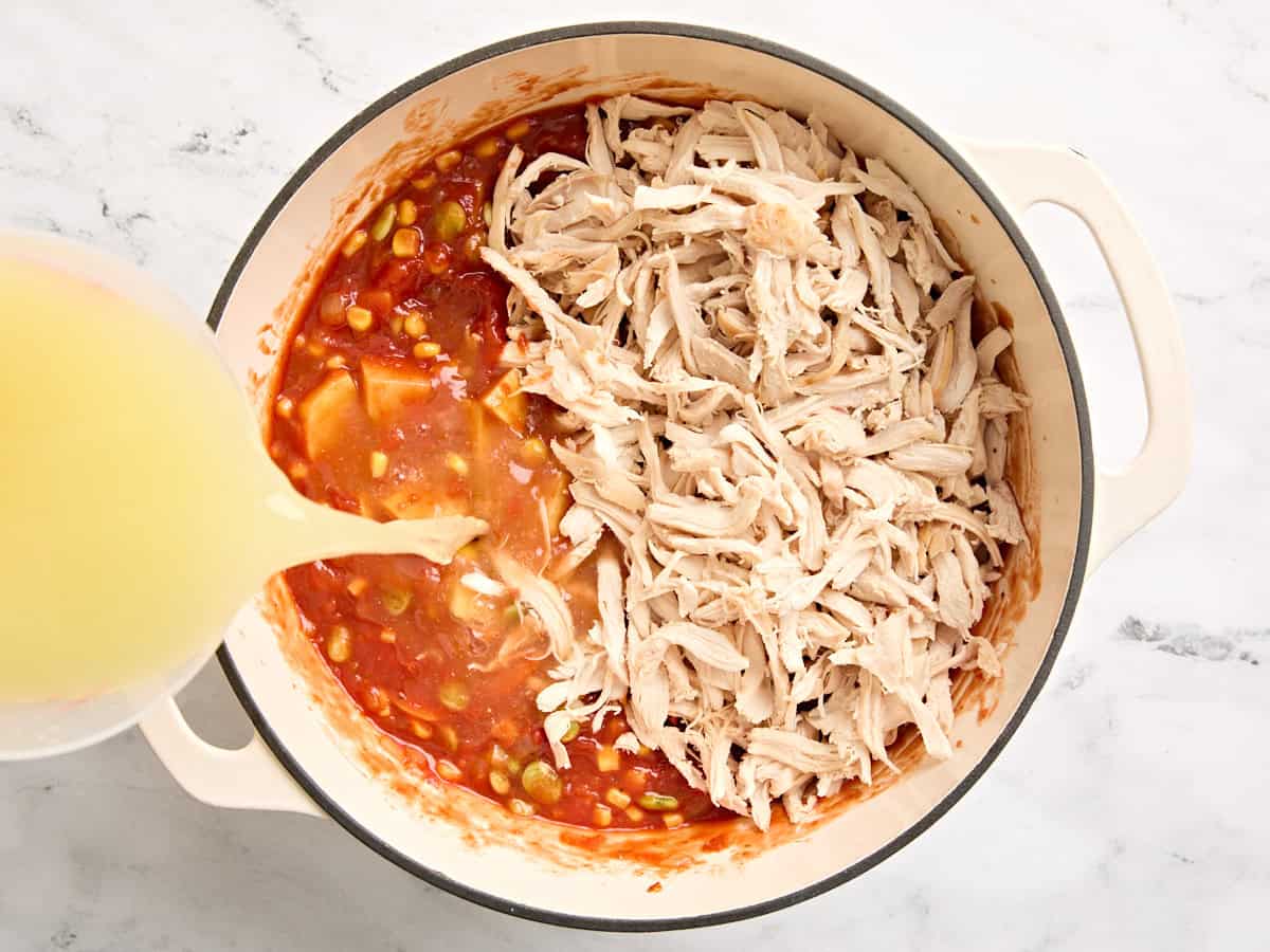 Broth and shredded chicken added to vegetables in a pot to make Brunswick stew.