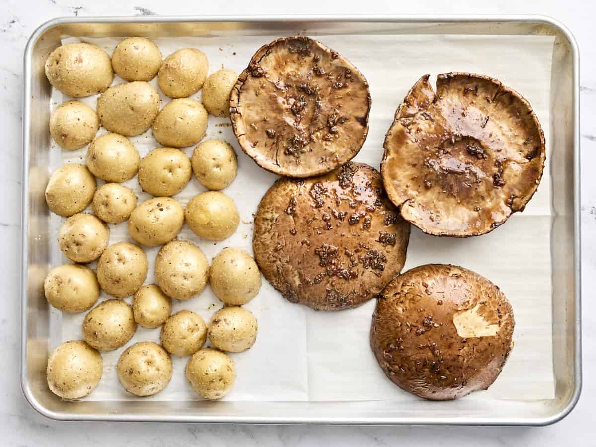 Roasted potatoes and marinading portobello mushroom caps on a sheet pan.