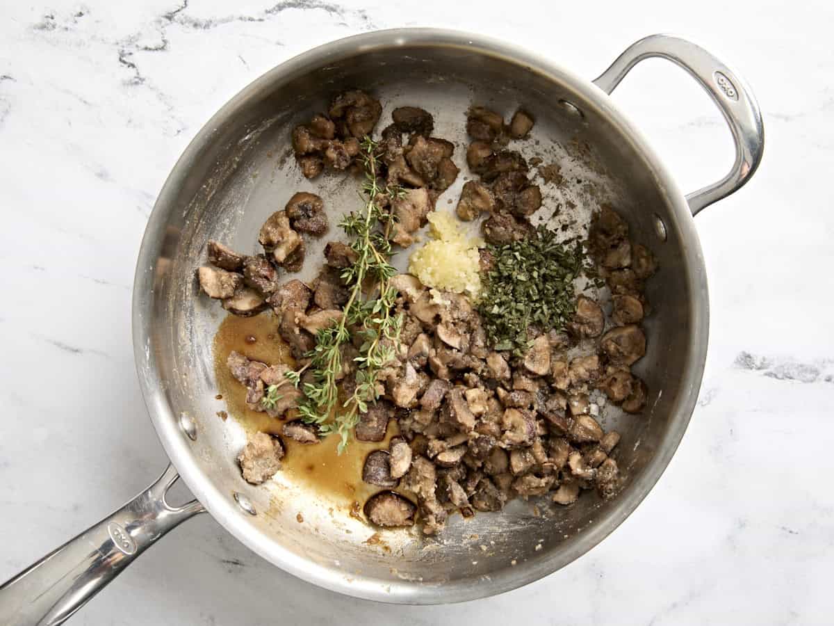 Garlic and herbs added to some flour coated mushrooms in a saute pan.