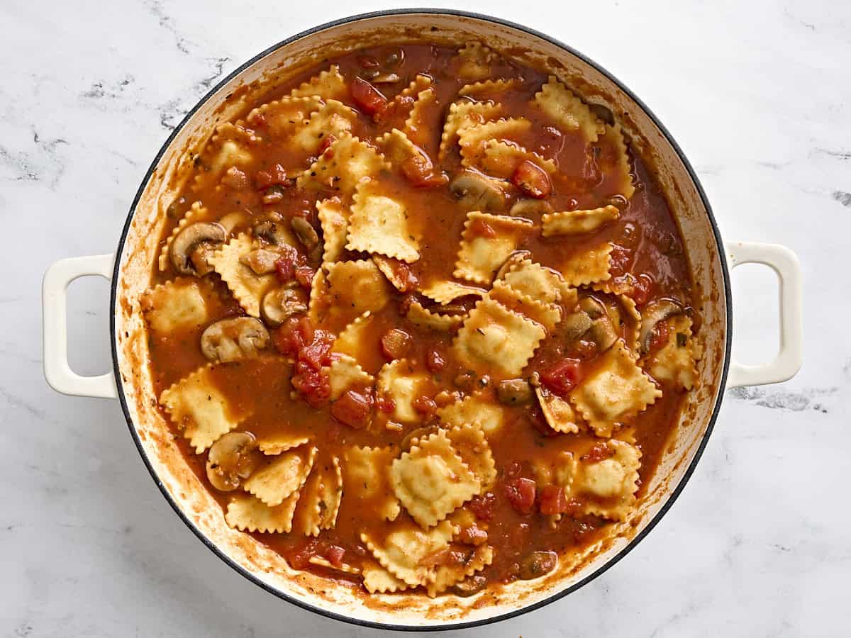 Cheese ravioli, sliced mushrooms, and tomato sauce in a skillet.