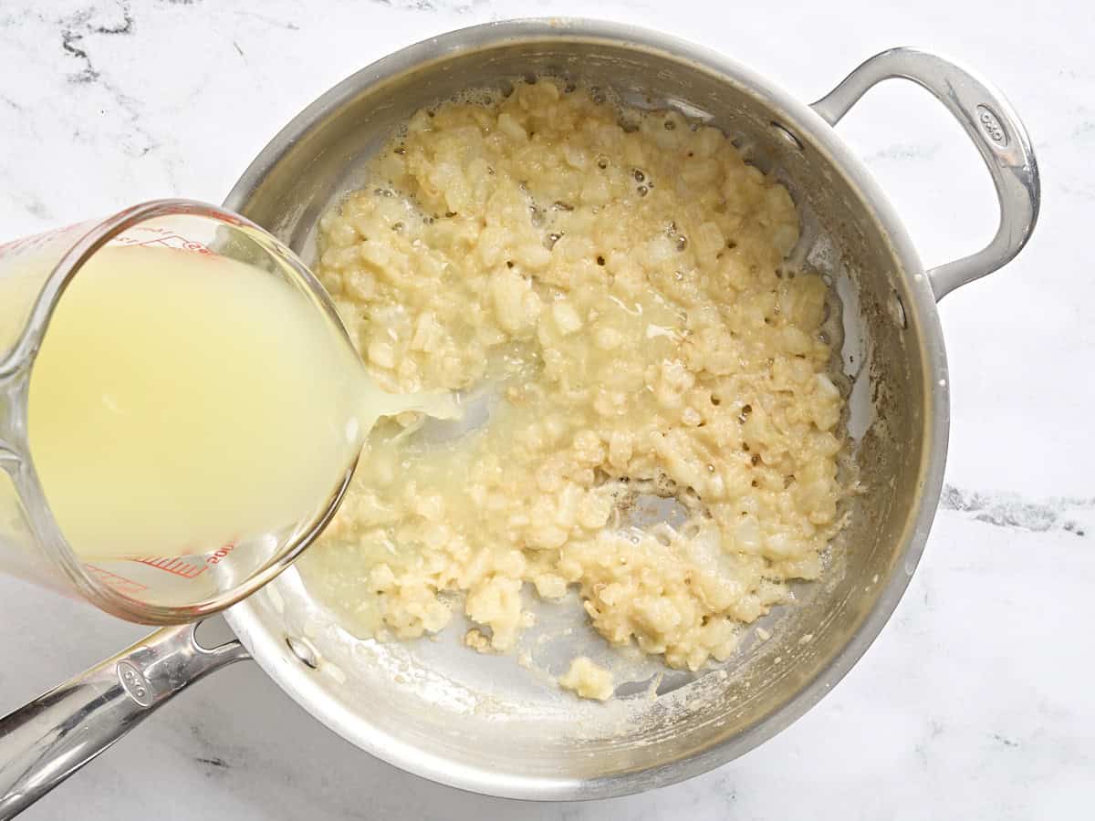 Chicken broth added to a golden roux in a skillet.