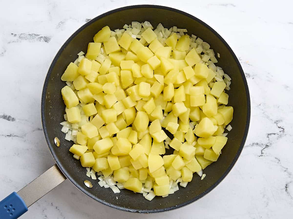 Diced potatoes added to diced onions in a skillet.