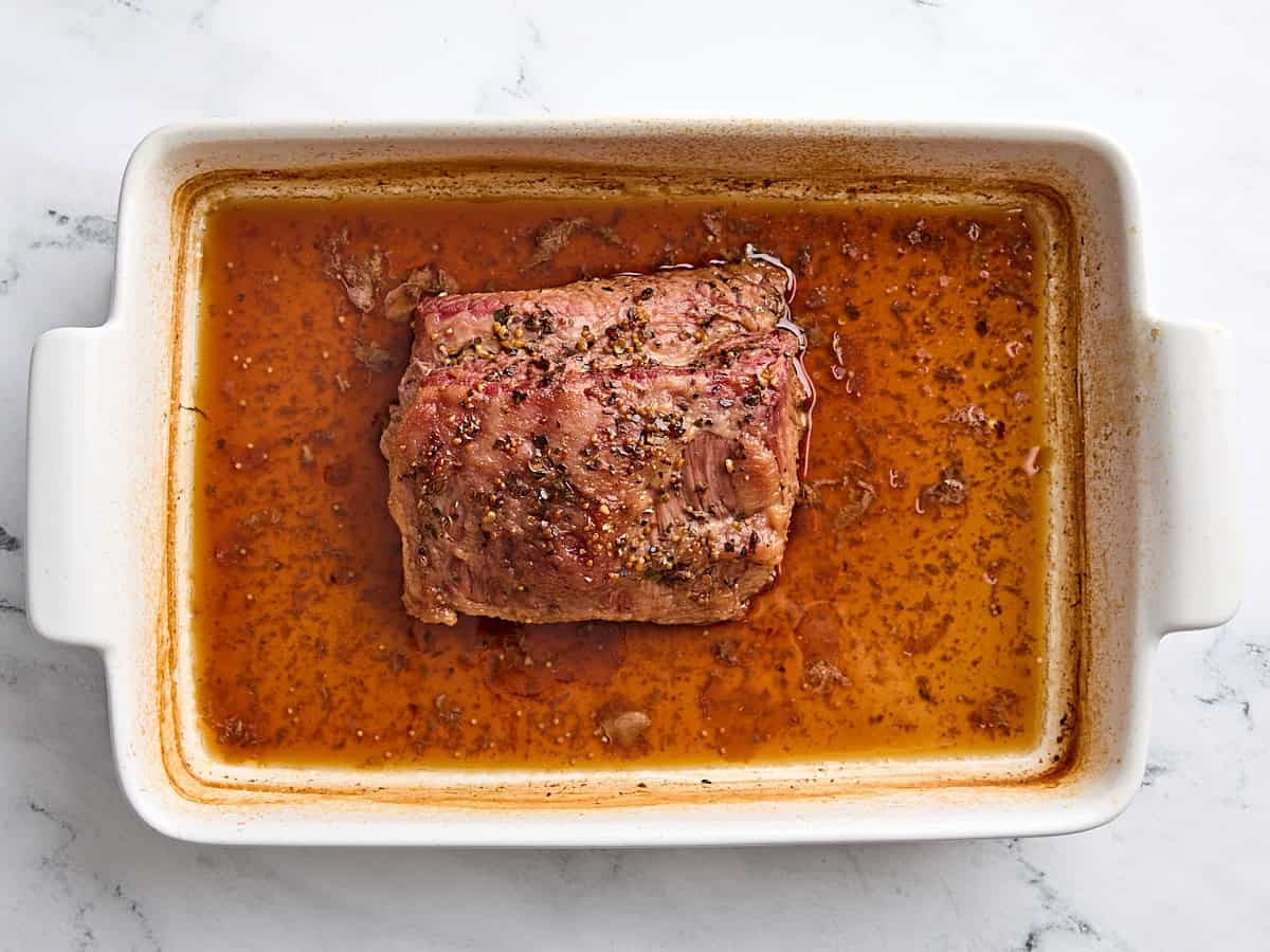 Cooked corn beef in a baking dish with beef broth.