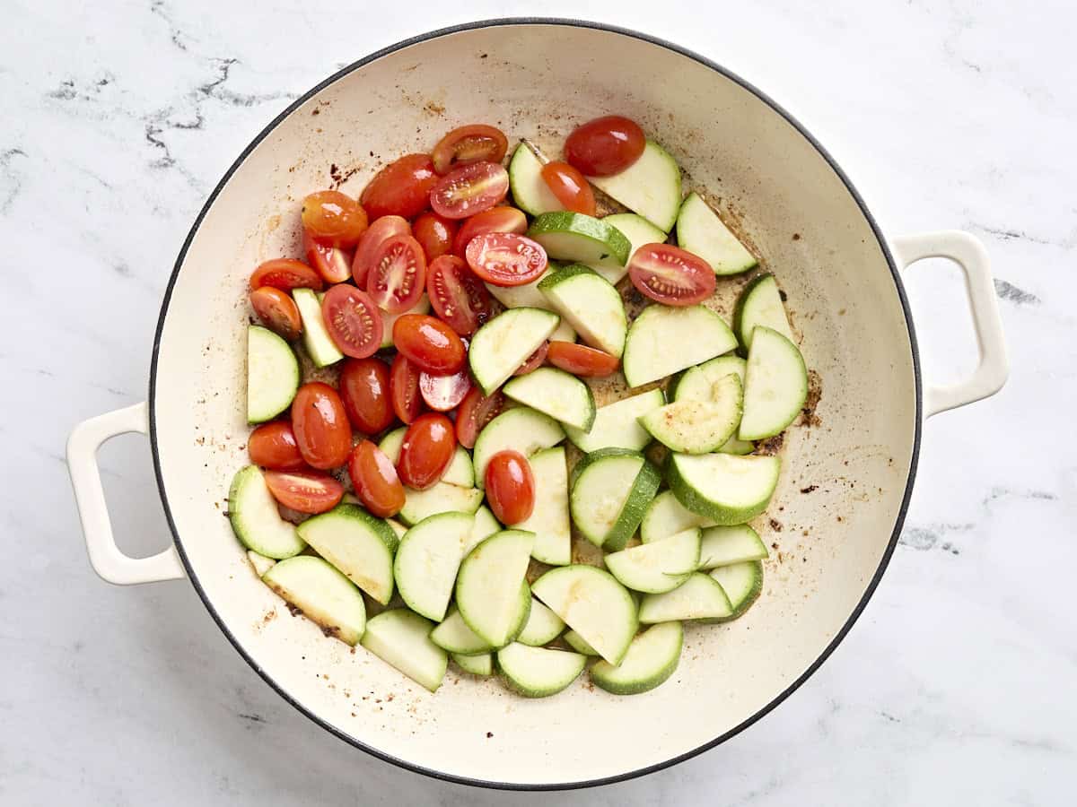 Sliced zucchini and grape tomatoes sauteing in a skillet.