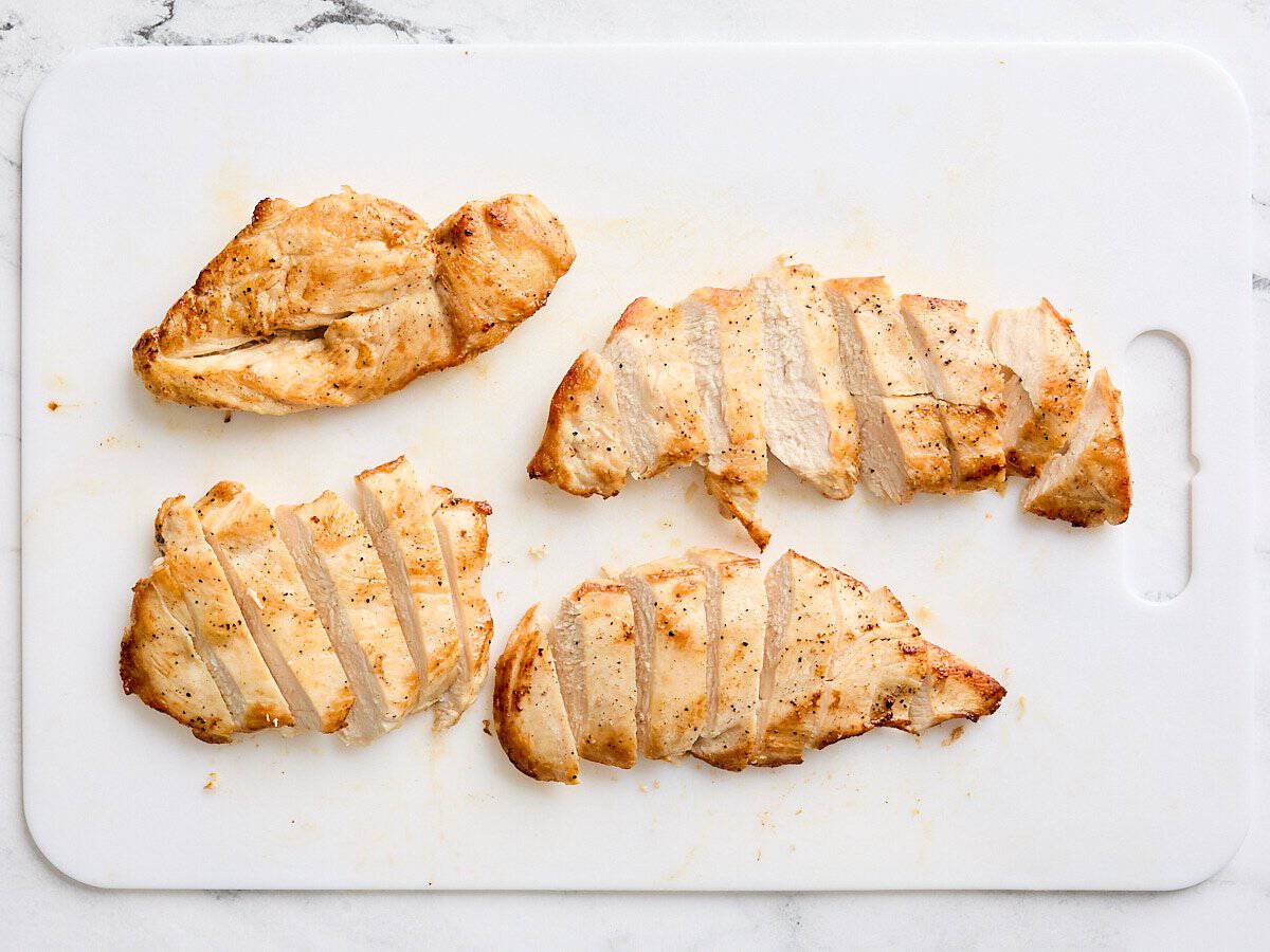 Cooked chicken breast cut into slices on a cutting board.