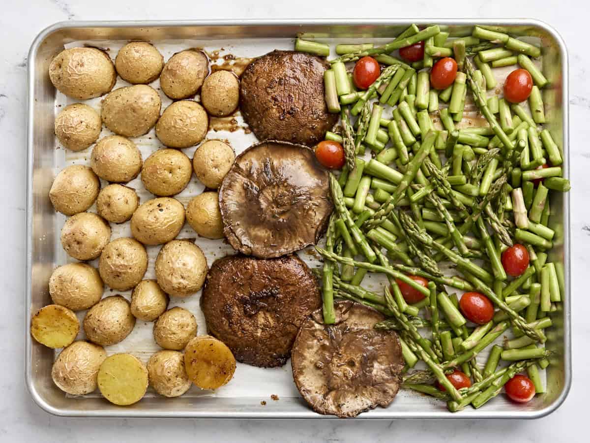 Potatoes, mushroom caps, chopped asparagus. and grape tomatoes on a sheet pan to make a one pan mushroom steak dinner.