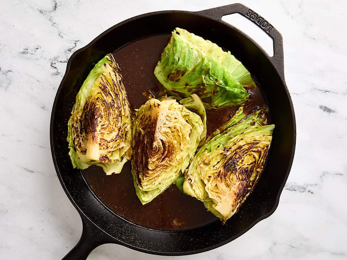 Cabbage steaks and sauce in a cast iron skillet before being baked in the oven.