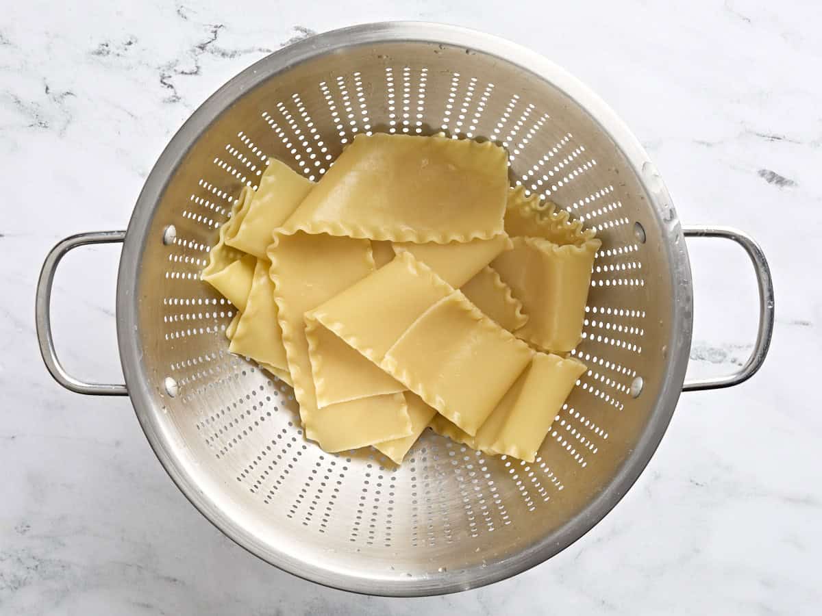 Cooked lasagna noodles draining in a strainer.