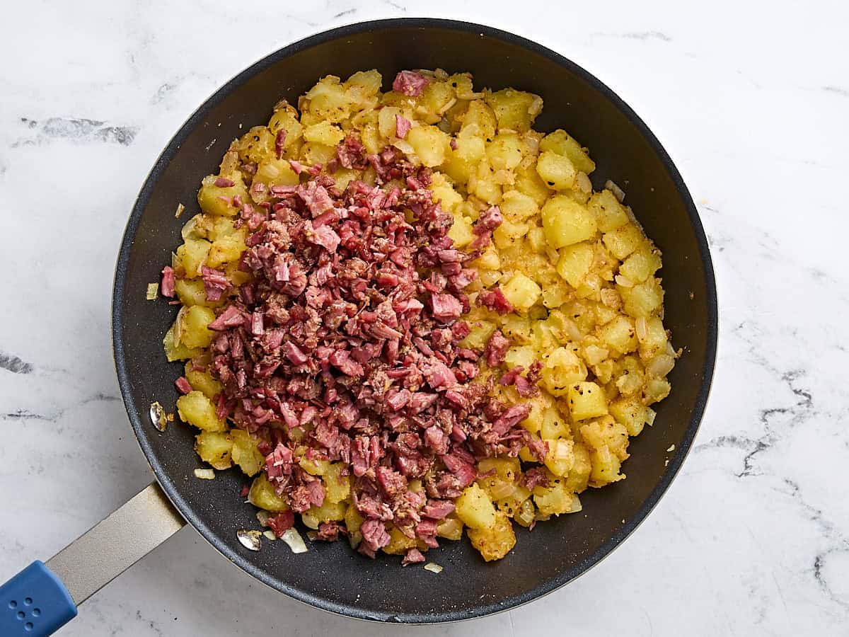 Chopped corned beef added to diced potatoes and onions in a skillet to make homemade corned beef hash.