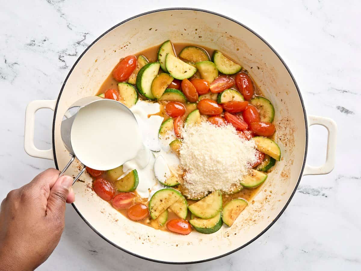 Heavy cream and grated Parmesan added to sauted zuchini and grape tomatoes in a skillet.