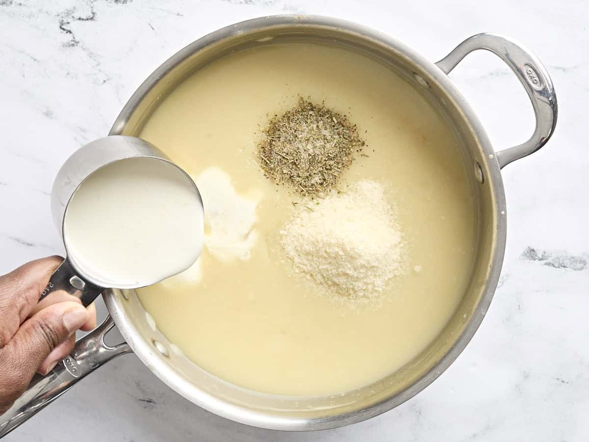 Seasoning, parmesan cheese, and heavy cream added to ricotta cheese sauce for white chicken lasagna in a baking dish.