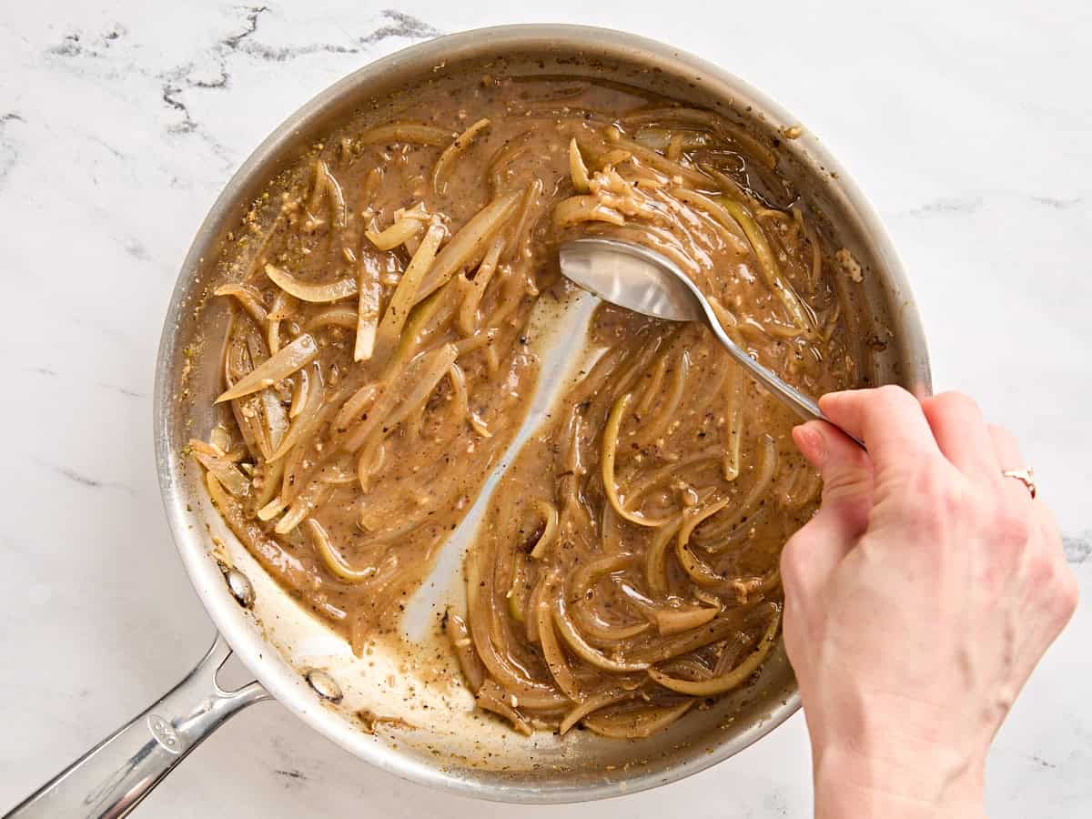 A spoon testing the thickness of onion gravy in a skillet.