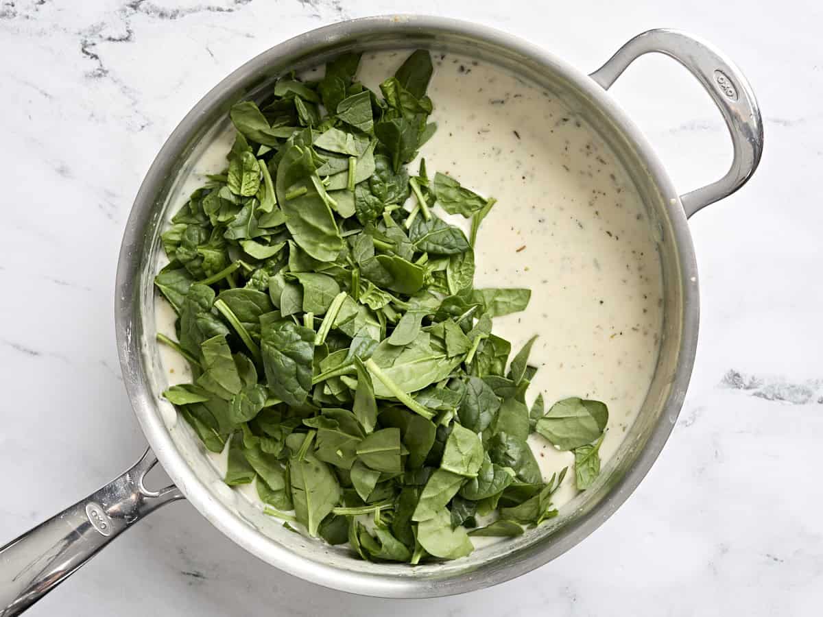 Fresh spinach added to ricotta cheese sauce in a skillet.