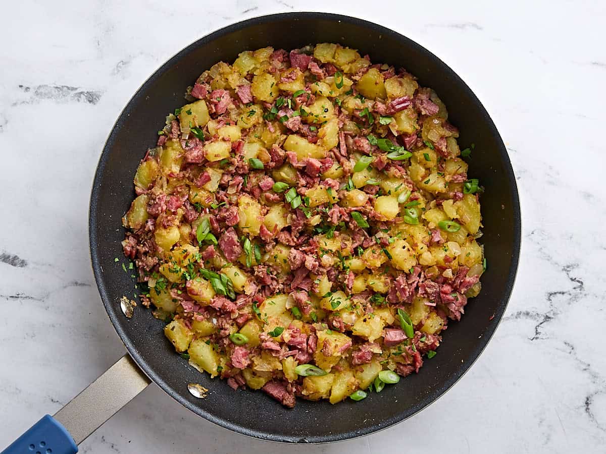 Finished corned beef hash in a skillet, topped with sliced green onions.