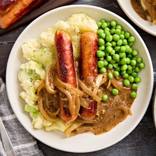 Overhead close up of bangers and mash on a plate with onion gravy and peas.