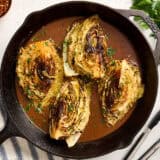 Overhead view of cabbage steaks and gravy in a cast iron skillet.