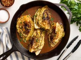 Overhead view of cabbage steaks and gravy in a cast iron skillet.