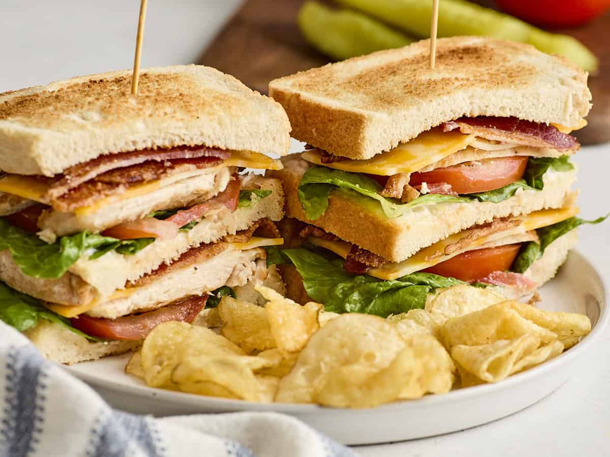 Close up side shot of a chicken club sandwich on a plate with chips.