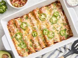 Overhead view of chicken enchiladas in a baking dish topped with fresh cilantro and sliced jalapenos.