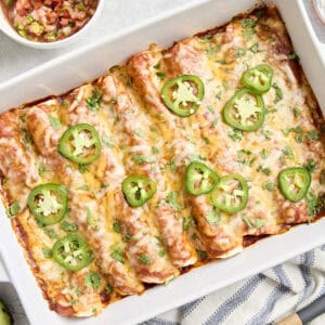 Overhead view of chicken enchiladas in a baking dish topped with fresh cilantro and sliced jalapenos.